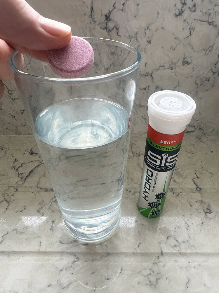 A SIS Berry electrolyte tablet being put into a glass of water