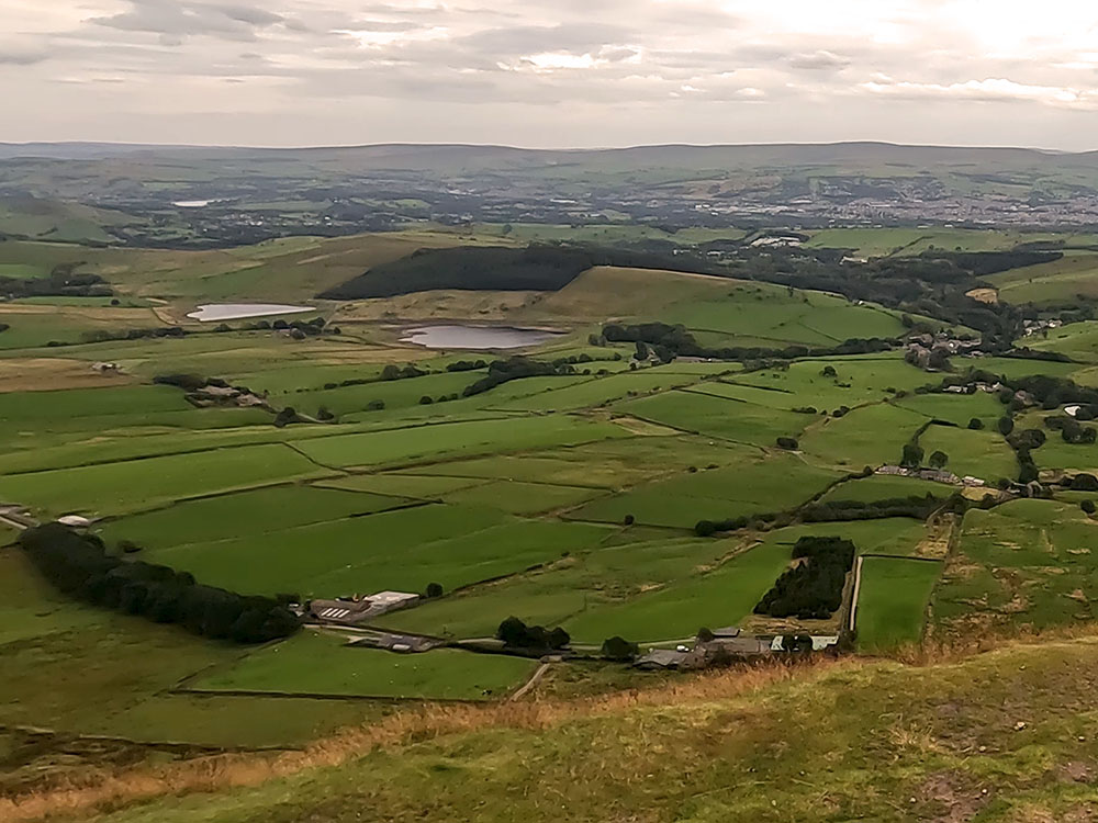 View from the summit of Pendle Hill, the Black Moss Reservoirs with Aitken Wood which houses the Pendle Sculpture Trail behind them