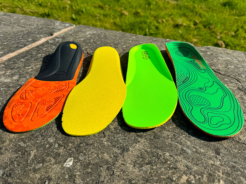 The top and bottom of a pair of Superfeet hike insoles, along with the pair of insoles that came with my Inov-8 hiking boots
