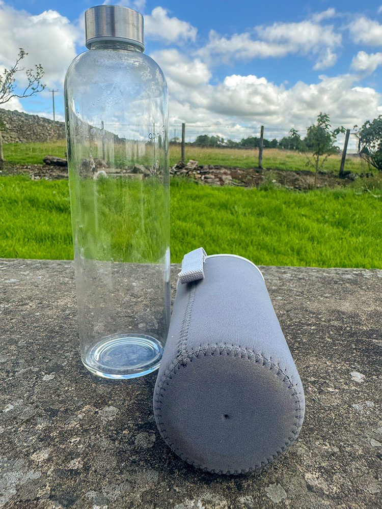 A glass water bottle and its accompanying silicon sleeve, in which it sits to help protect it