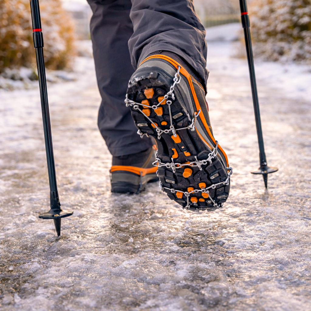 Walker using trekking poles and microspikes on an icy path