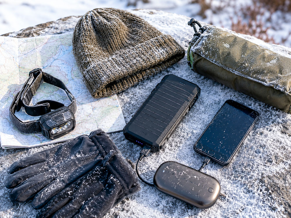 Winter walking essentials with a power bank, head torch, hand warmer, gloves and map for cold-weather battery backup.