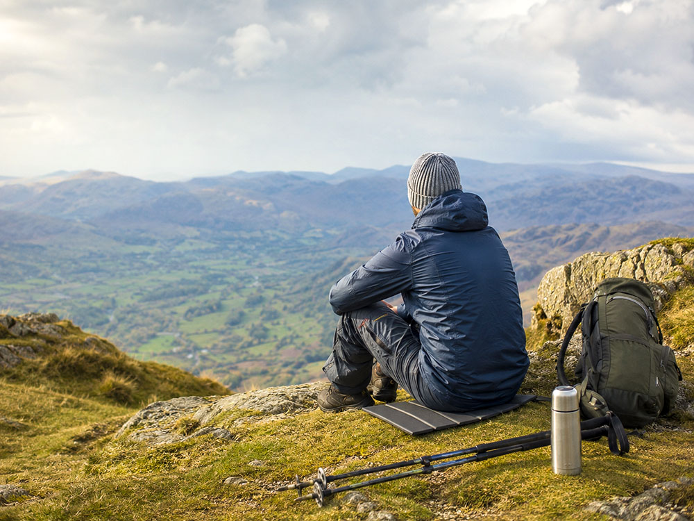 Walker sitting on a compact folding sit mat during a UK hillwalking break, with rucksack, flask and mountain view in the background.