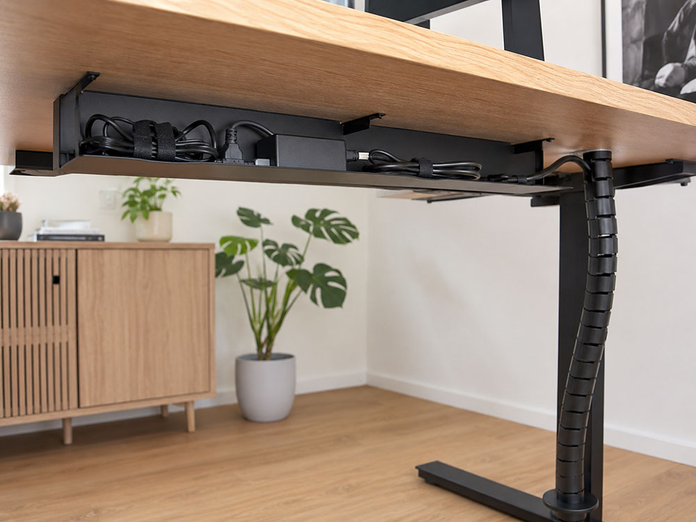 Under-desk cable tray holding power cables neatly under a standing desk with cable spine to the floor.