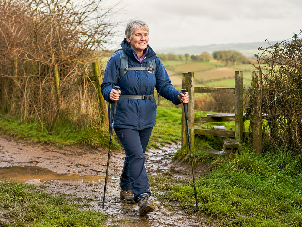 Older walker using two walking poles on a muddy countryside path, showing how poles can add confidence on uneven ground.
