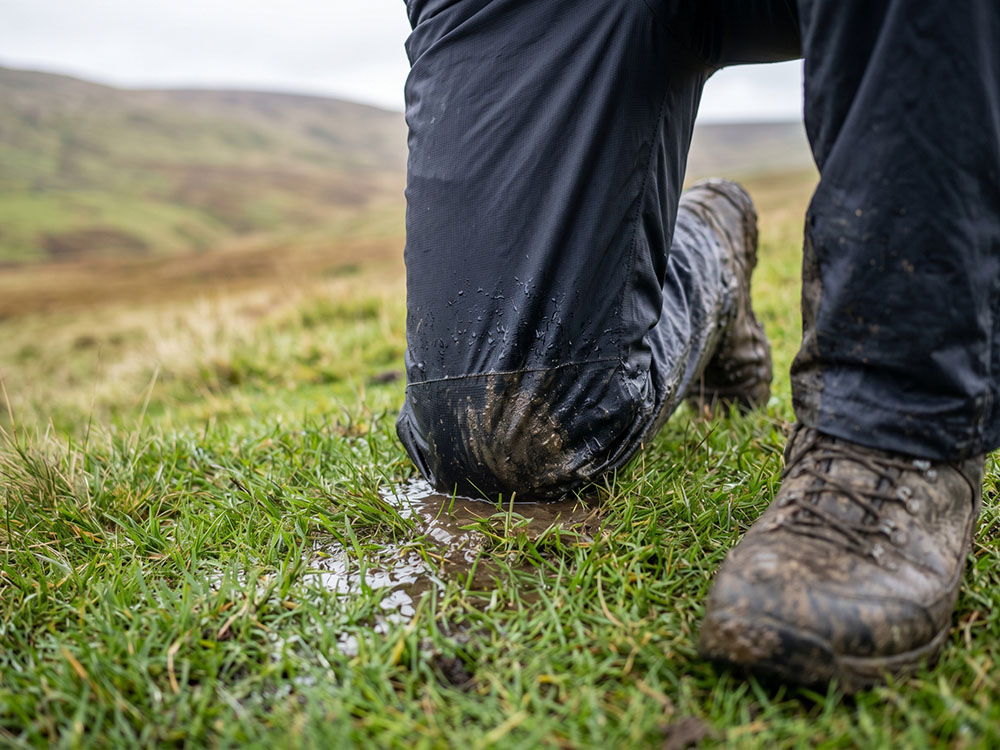 Close-up of a walker kneeling on wet grass in waterproof overtrousers to show pressure on the knee area