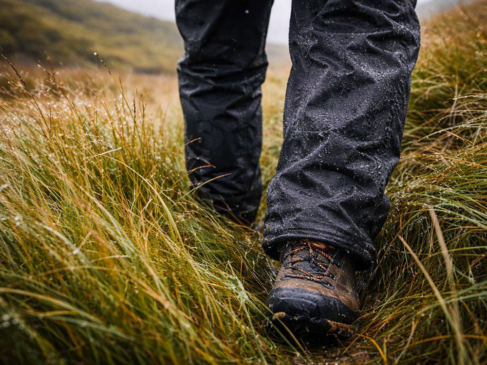 Close-up of a walker moving through long wet grass in waterproof overtrousers