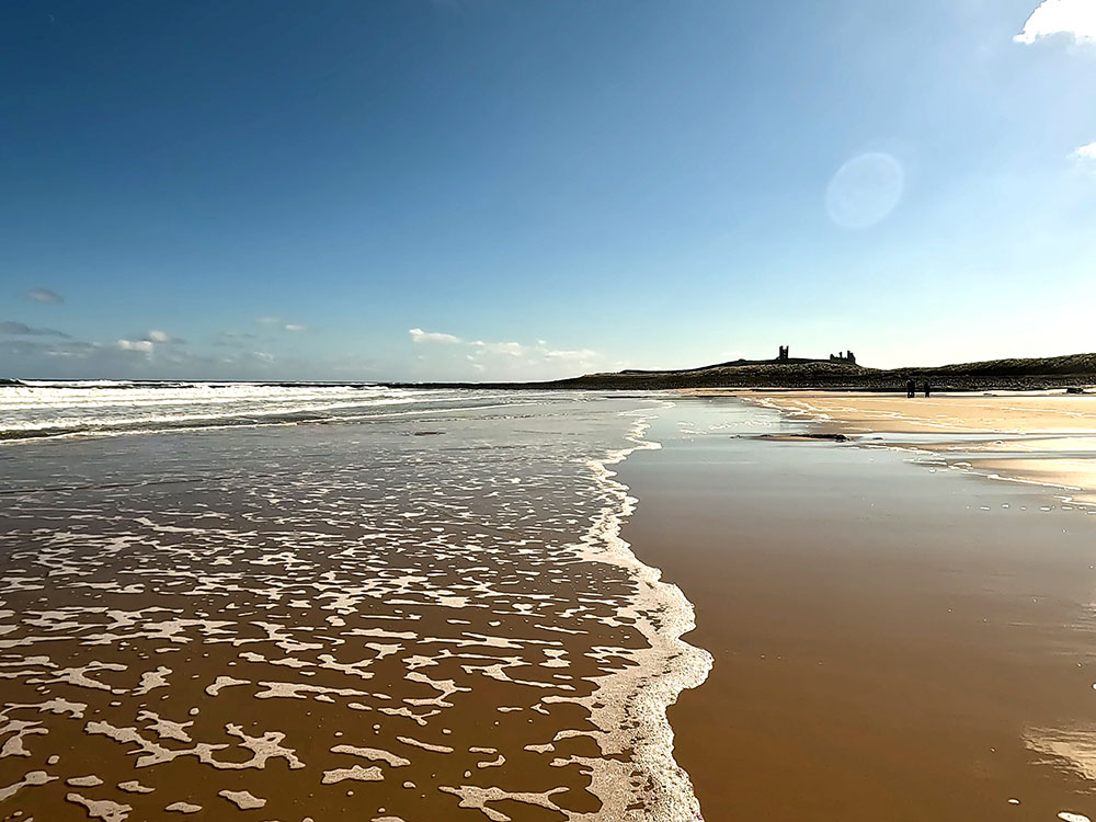 Looking back along the beach at Embleton Bay towards Dunstanburgh Castle