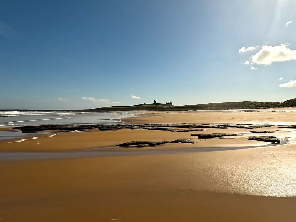 Walking along Embleton Bay sands in the direction of Dunstanburgh Castle