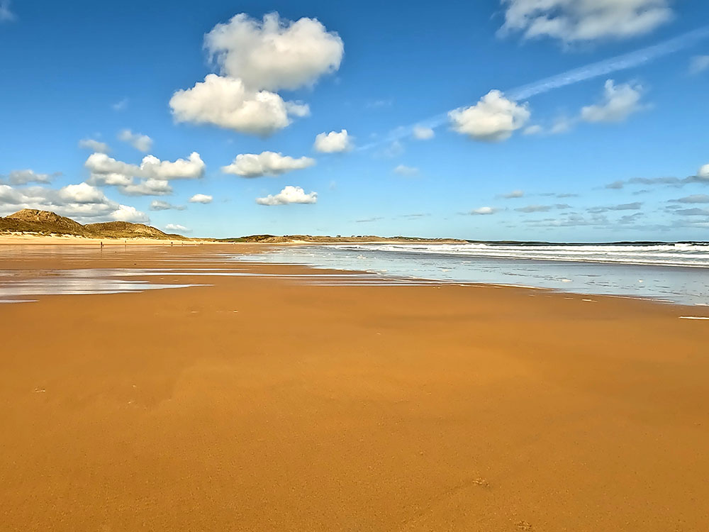 Walking along the sandy beach looking towards the sand dunes at Embleton Bay