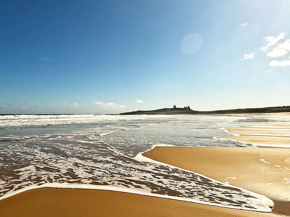 Walking back along the beach at Embleton Bay with Dunstanburgh Castle on the horizon