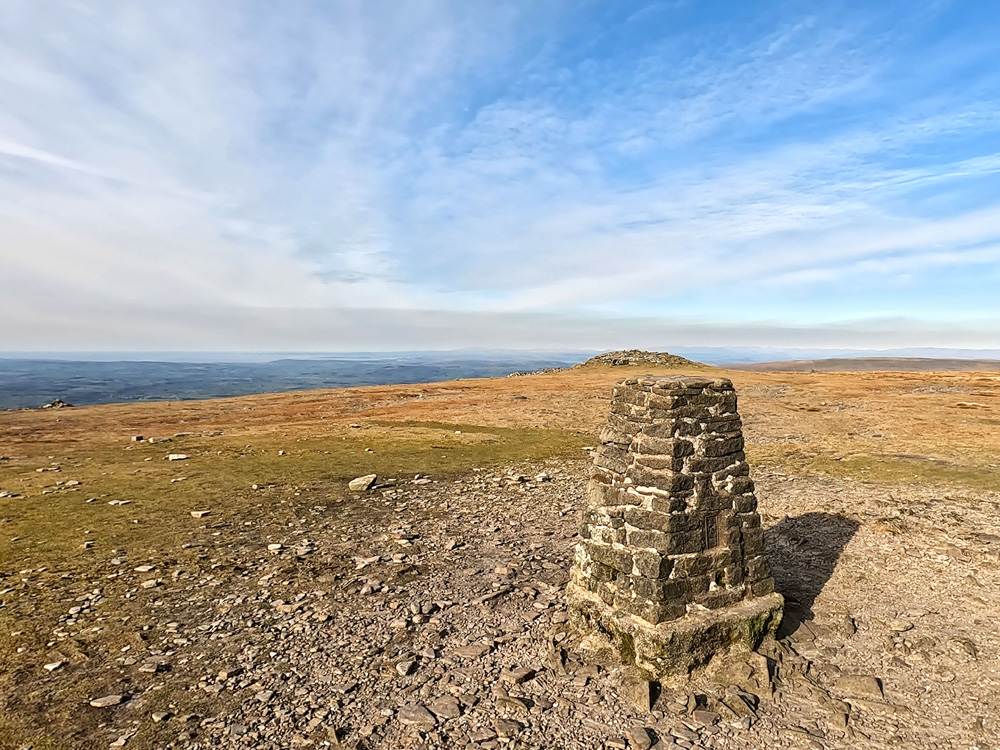 The Lakeland Fells over the trig point on Ingleborough summit