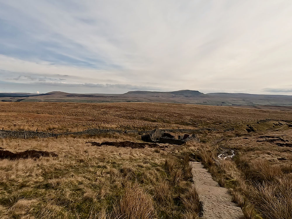 The flagged path leading down to ruins of shooting hut with Pen-y-ghent on the horizon