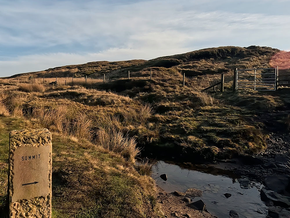 Stone summit marker and gate leading up onto flagged section to the summit