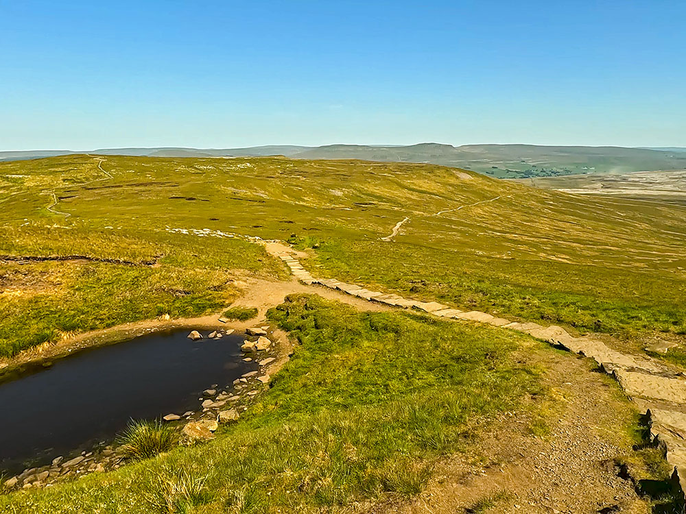 Flagged path passing by a small tarn as it starts heading across Simon Fell Breast