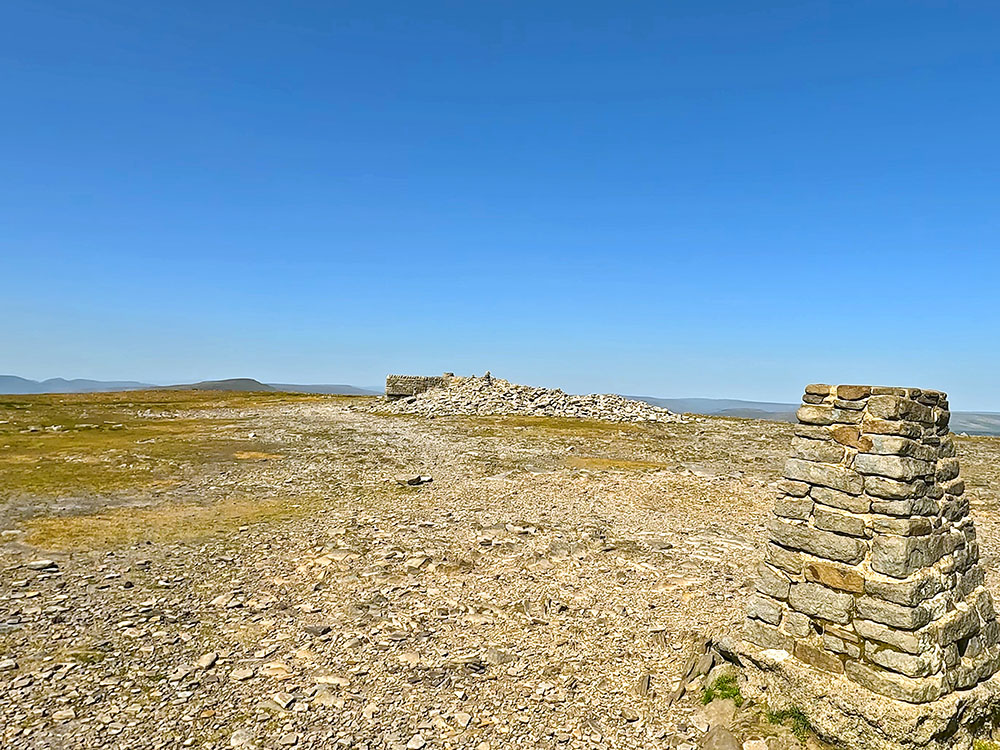Looking over the trig point on Ingleborough over the weather shelter and Whernside towards the Howgills