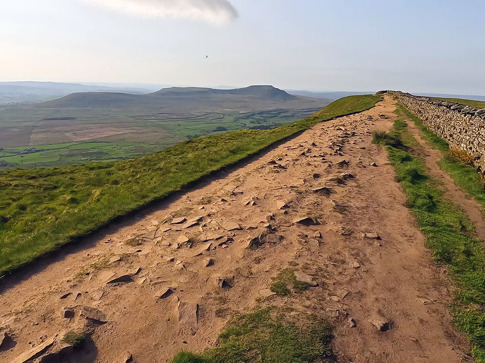 Path by the side of the wall approaching Whernside summit, with Ingleborough ahead and Ribblehead Viaduct below