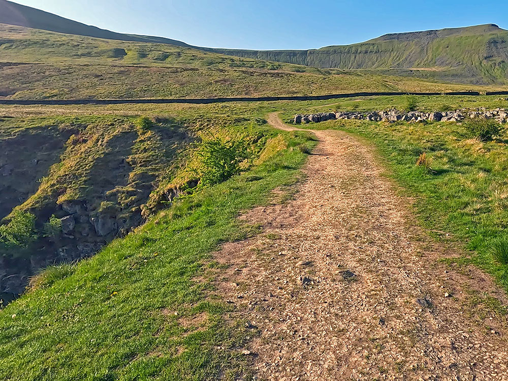 Path heading by the entrance to Braithwaite Wife Hole cave with Ingleborough ahead