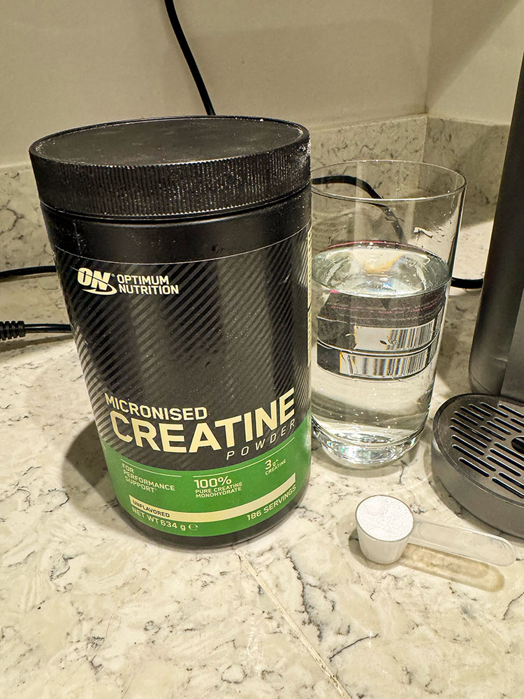 Minimal product photo showing creatine powder, scoop and glass of water on a counter