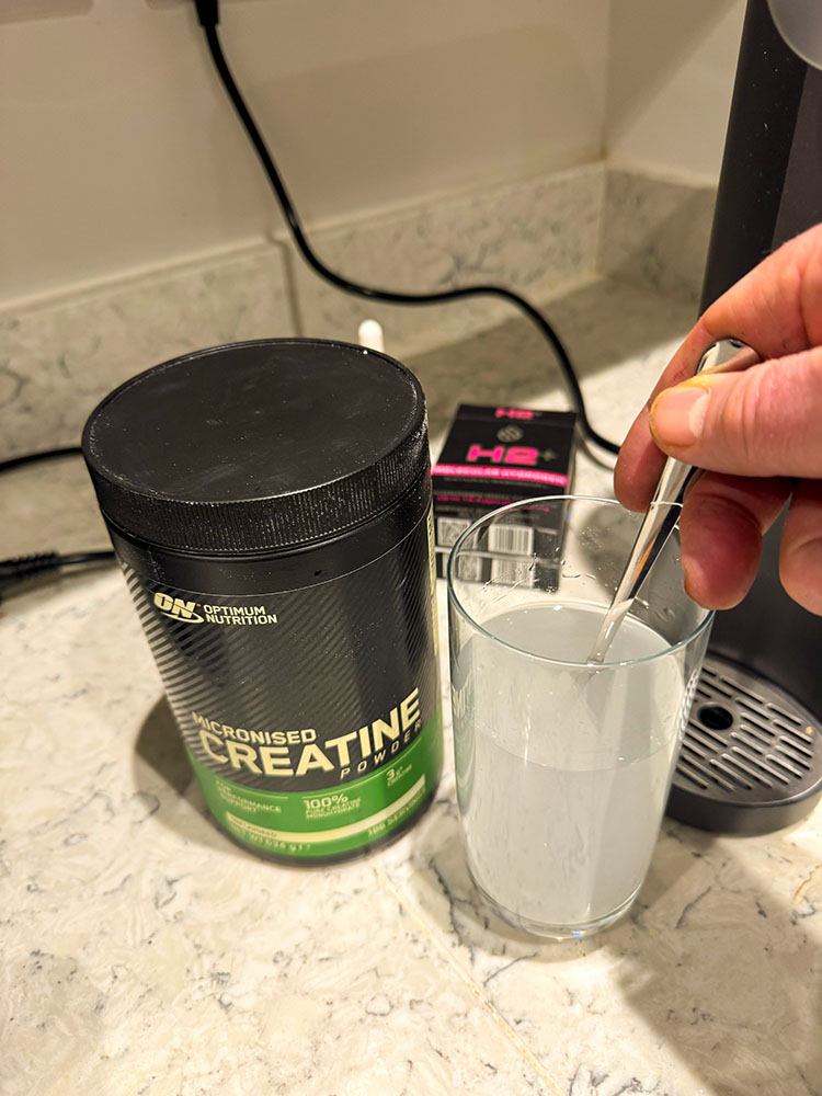 Close-up of a woman mixing creatine powder into a water bottle in a bright kitchen
