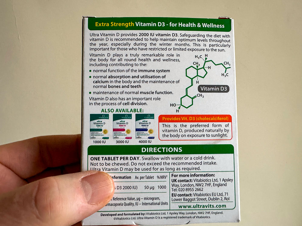 Close-up photo of hands reading a supplement label to check vitamin D dose in IU and micrograms and avoid accidental double dosing