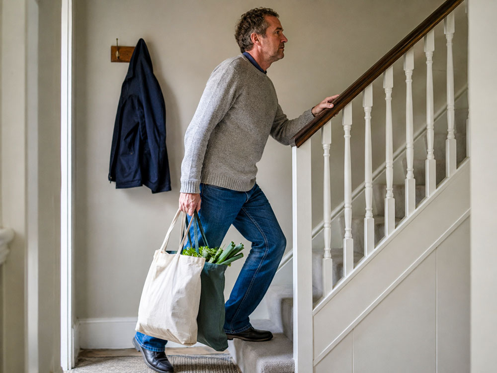 Man carrying bags of groceries upstairs at home, illustrating non-exercise activity thermogenesis from ordinary daily movement.