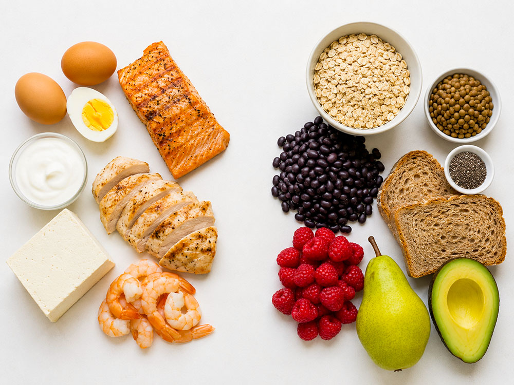 Flat lay of eggs, salmon, chicken, yoghurt, tofu, prawns, oats, beans, lentils, wholegrain bread, berries, pear, avocado and chia seeds.